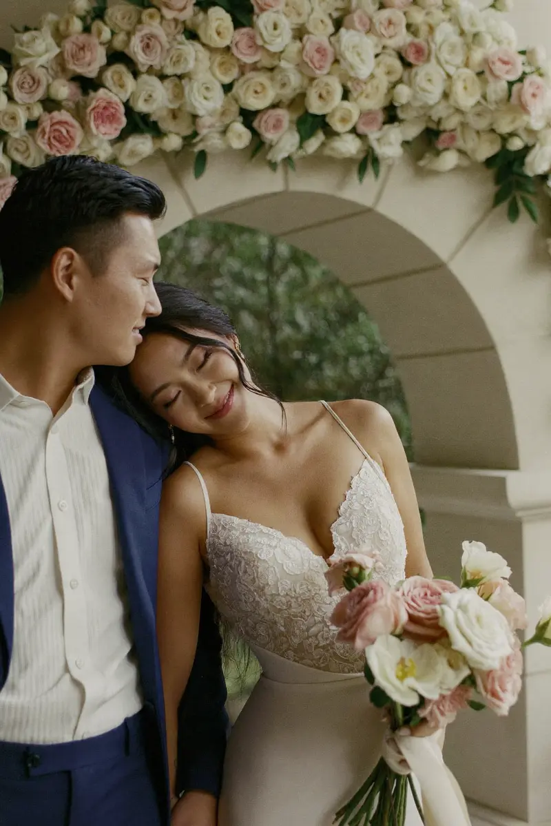 A bride and groom, close together under an arch of roses
